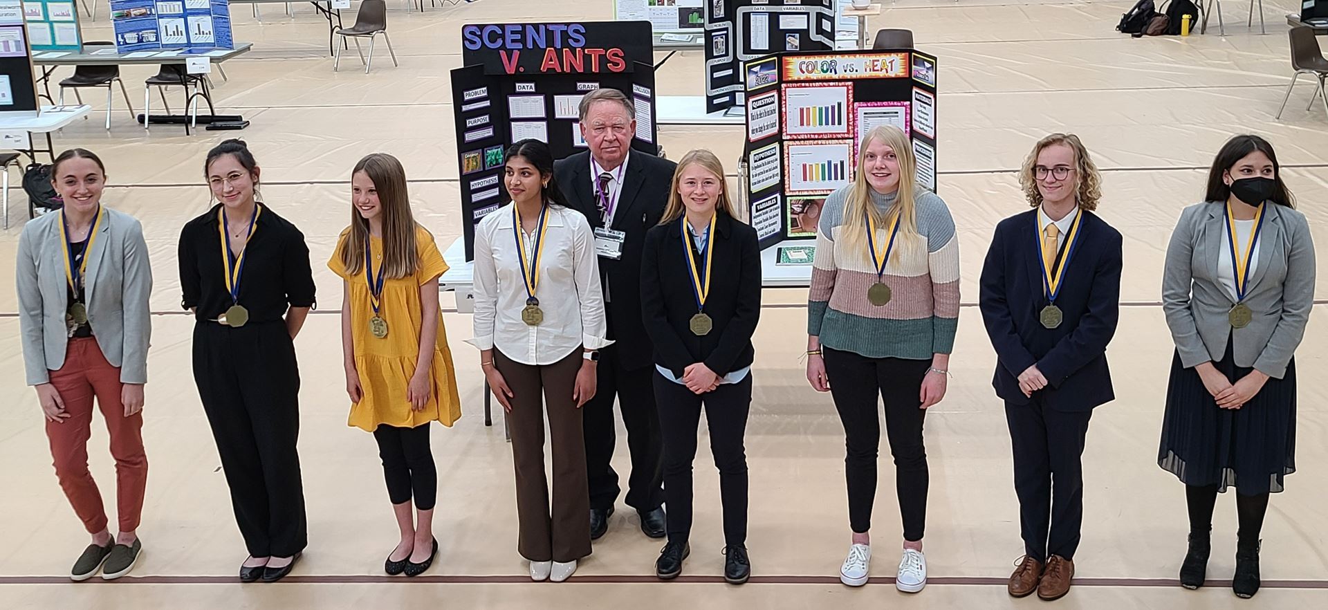 photo 8 ninth to twelfth grade students posing for photo with medals won for being the Nebraska state science fair high school 2022 winners. Students mentor president of the Nebraska Junior Academy of Science stands behind them  